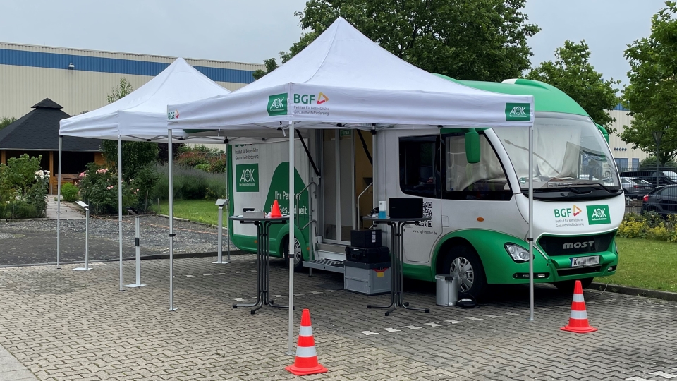 Ein Impfmobil der AOK steht auf einem Parkplatz, davor sind Pavillons aufgestellt